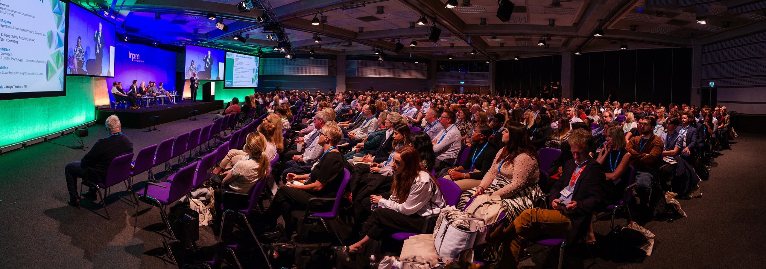 A wide angle photo of people on stage and people sitting listening at a property managers industry event